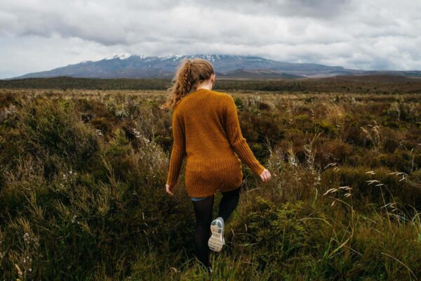 A woman in an orange dress walking through the grass.